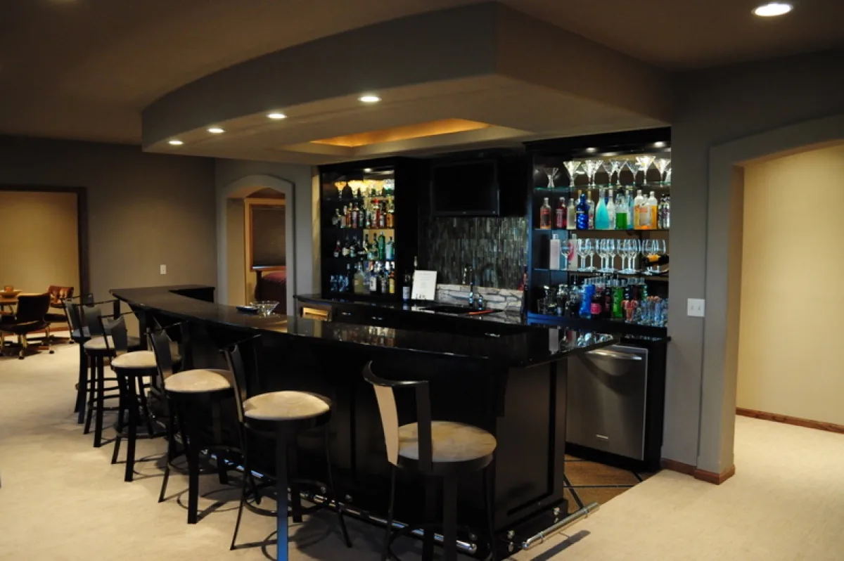 A custom bar with a granite counter, dark cabinetry, and lit display shelving