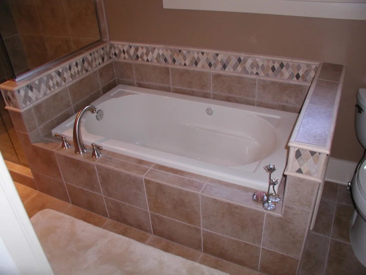 A tiled tub deck with a mosaic accent band and a glass shower alongside