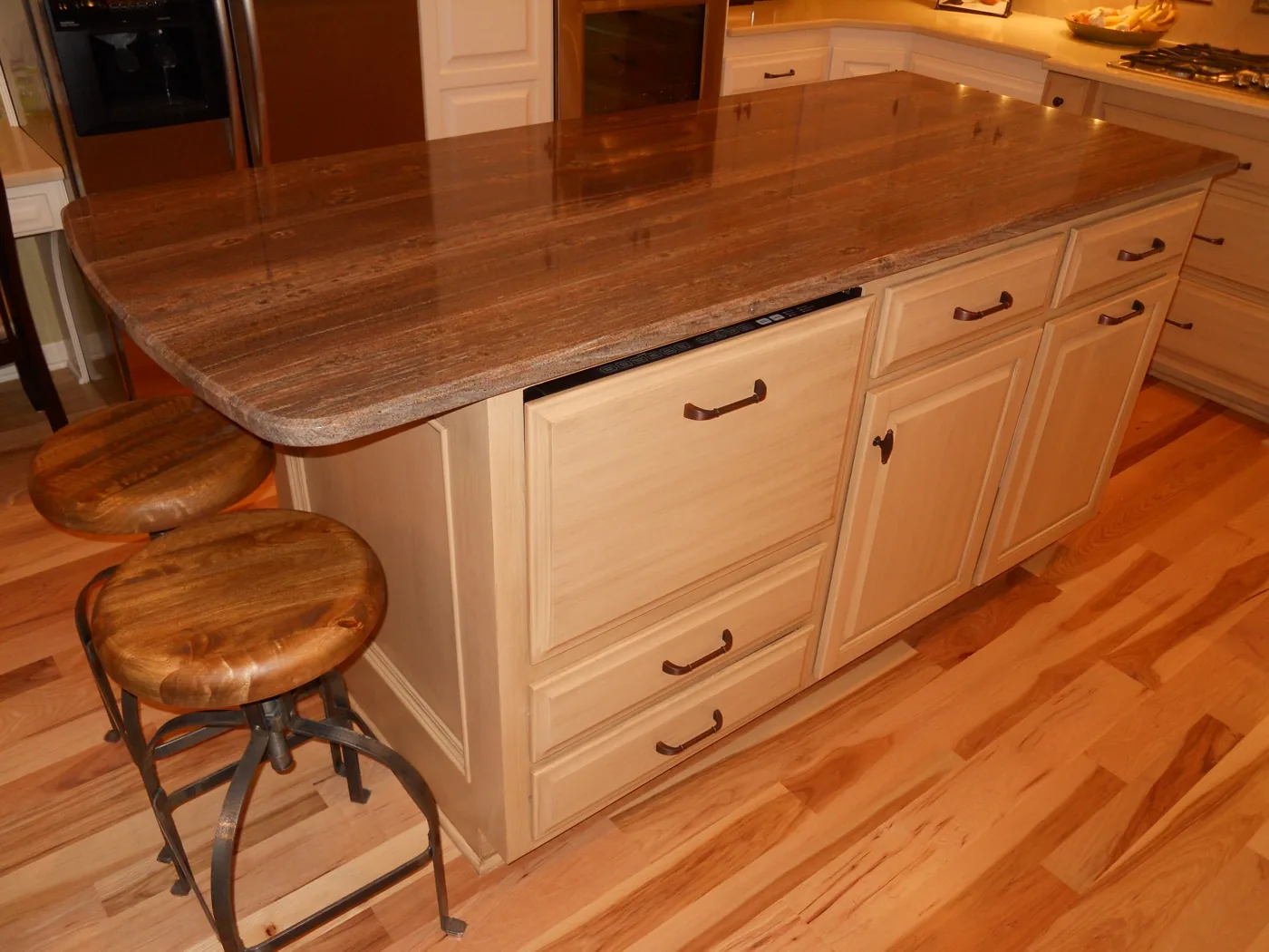 A kitchen island in light glazed cabinetry with a brown granite top and two stools
