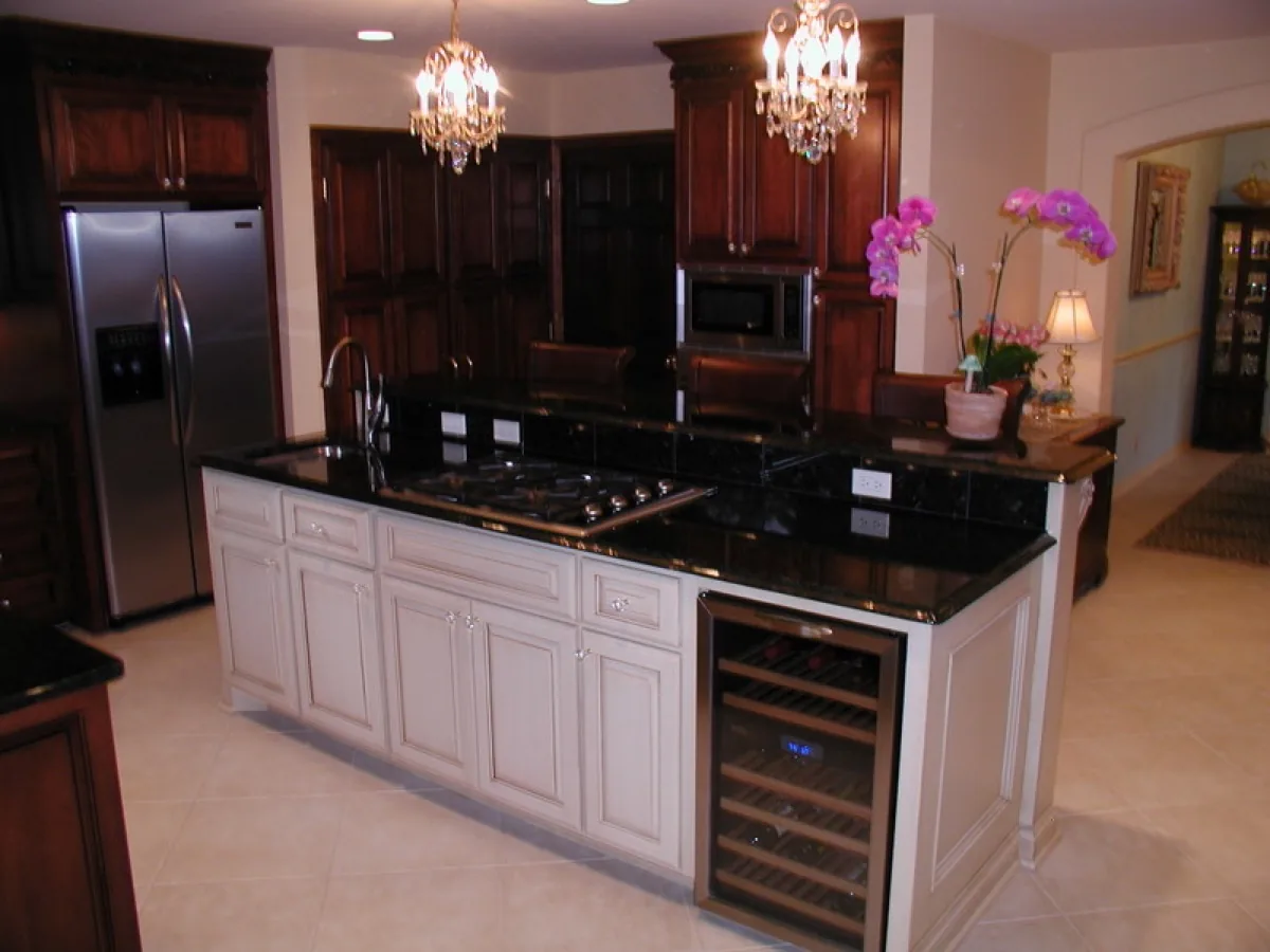 A remodeled kitchen with a glazed island, black granite counters, and two chandeliers
