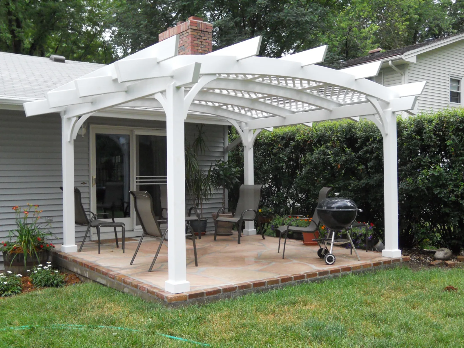 A white pergola over a flagstone patio beside the house